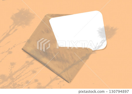 Natural light casts shadows from wildflowers on an envelope with a sheet of white paper lying on an orange background. Mockup Natural light casts shadows from wildflowers on an envelope with a sheet of white paper lying on an orange background. Mockup 130794897