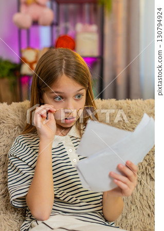 Child girl kid pretending to read documents in adult glasses sitting on home sofa at living room Child girl kid pretending to read documents in adult glasses sitting on home sofa at living room 130794924