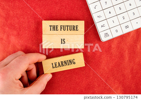 Concept of Intelligence, science and mind. THE FUTURE IS LEARNING assembled from blocks in a composition with part of a white calculator and a hand, top view 130795174