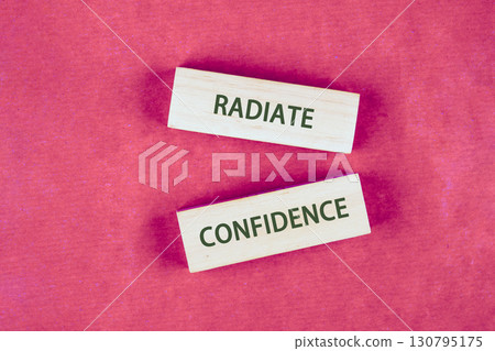 Concept words RADIATE CONFIDENCE assembled from blocks on a crimson background, top view 130795175