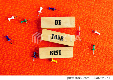Business motivational concept. Copy space. Words BE YOUR BEST assembled from wooden blocks in a composition with stationery pins on an orange provocative background, top view 130795234