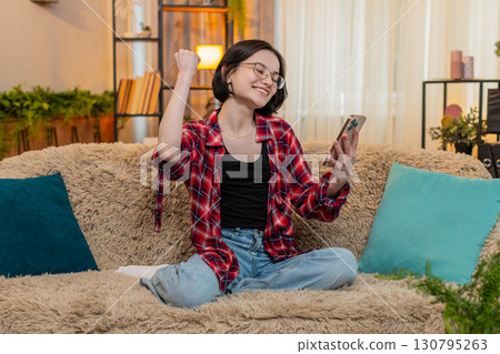 Happy smiling woman using smartphone at home winning online lottery game celebrating jackpot victory 130795263