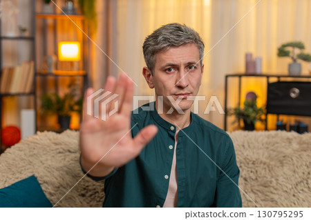 Young man shows stop gesture with raised hand strict face expressing emotional boundary or rejection Young man shows stop gesture with raised hand strict face expressing emotional boundary or rejection 130795295
