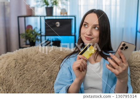 Young woman holding credit card and smartphone making online purchase happily satisfied shopping 130795314