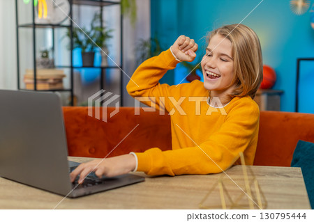 Teenager boy enthusiastically playing online game on laptop, celebrating victory on couch at home Teenager boy enthusiastically playing online game on laptop, celebrating victory on couch at home 130795444