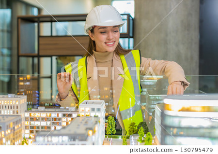 Confident young female architect in hardhat analyzing office complex architectural model in office 130795479