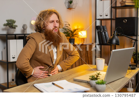 Ill sick man feeling overeating pain touching stomach during work process on laptop in home office Ill sick man feeling overeating pain touching stomach during work process on laptop in home office 130795487