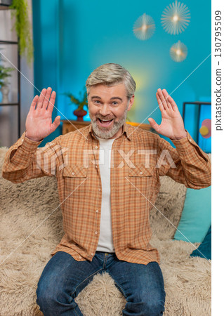 Mature man smiling friendly sitting on cozy sofa waving hand in greeting hello, hi at home room Mature man smiling friendly sitting on cozy sofa waving hand in greeting hello, hi at home room 130795509