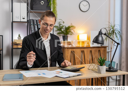 Successful businessman analyzing financial report while using calculator sitting at home office desk Successful businessman analyzing financial report while using calculator sitting at home office desk 130795512