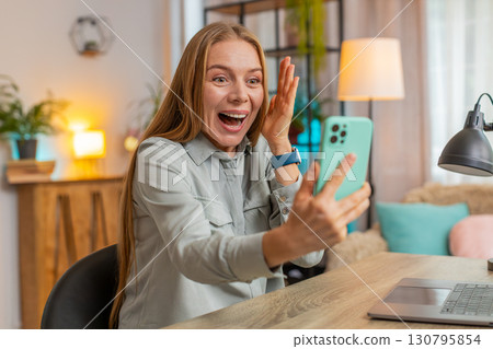 Happy mature woman freelancer using smartphone celebrating success victory winning lottery at table Happy mature woman freelancer using smartphone celebrating success victory winning lottery at table 130795854