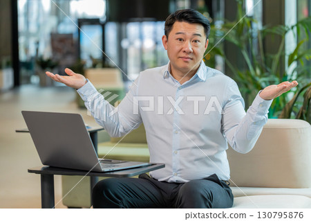 Angry businessman raising hands in indignant expression, asking reason of failure in office lobby 130795876