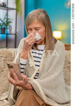 Mature woman covered with blanket on sofa, ill and sick, using smartphone to order medicine at home Mature woman covered with blanket on sofa, ill and sick, using smartphone to order medicine at home 130795906