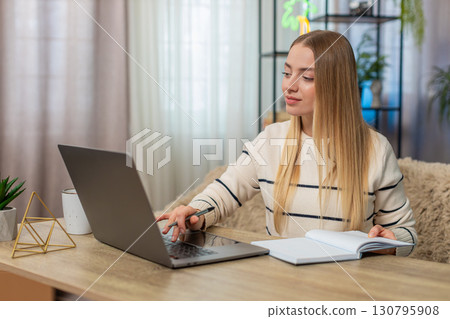 Caucasian woman smiling, finding inspiration at home on table, typing on laptop, remote education 130795908