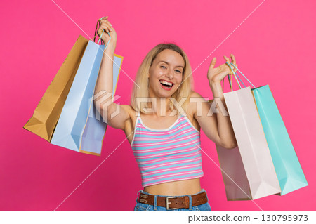 Woman showing shopping bags advertising purchase discounts smiling looking amazed with low prices Woman showing shopping bags advertising purchase discounts smiling looking amazed with low prices 130795973