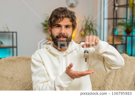 Happy Indian man real estate agent sitting on sofa showing the keys of new home house apartment Happy Indian man real estate agent sitting on sofa showing the keys of new home house apartment 130795983