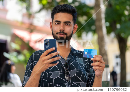Indian man using credit bank card smartphone transferring money purchases online shopping outdoors Indian man using credit bank card smartphone transferring money purchases online shopping outdoors 130796082