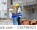 Tow young constructions woman in vest with yellow helmet working with laptop and holding radio while standing on building construction site. Home building project. 130796923