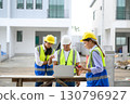 Group of contractors, engineers and formats in safety vests with helmets working with laptop, standing on under-construction building site. Home building project. Engineer foreman discusses with a 130796927