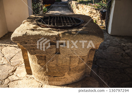 Ancient stone well with carved cross and metal grate, symbolizing history and spirituality in a traditional courtyard setting. Ancient stone well with carved cross and metal grate, symbolizing history and spirituality in a traditional courtyard setting. 130797294