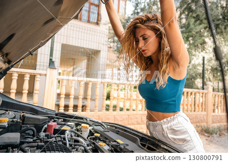 Young woman checking car engine with hood open 130800791