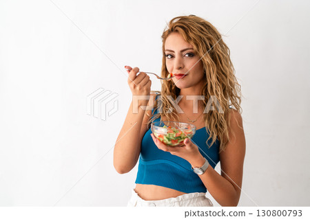 Young woman eating fresh vegetable salad 130800793