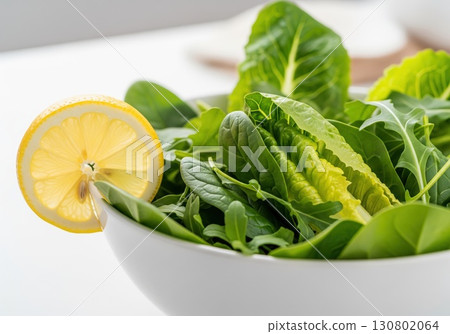 Clean bowl featuring leafy salad greens topped with lemon slice against minimal backdrop highlighting bright natural tones and nutritious health focus concept Clean bowl featuring leafy salad greens topped with lemon slice against minimal backdrop highlighting bright natural tones and nutritious health focus concept 130802064