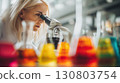 Scientist examining samples through microscope surrounded by colorful lab glassware 130803754