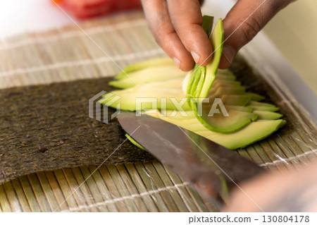A sushi chef's hands skillfully preparing a fresh salmon, tuna, and avocado roll 130804178