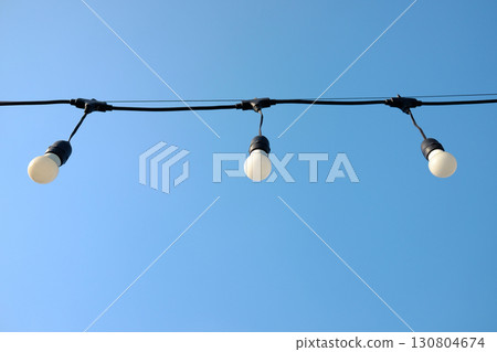 Vintage glowing light bulbs hang from a thin wire in the air and blu sky in bright day Vintage glowing light bulbs hang from a thin wire in the air and blu sky in bright day 130804674