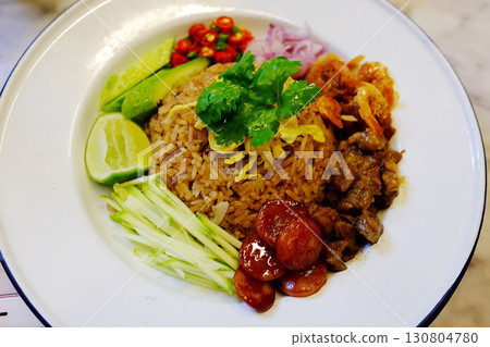 Thai mixed rice and stir fry with shrimp paste and sweet pork and assorted condiments on white dish. traditional of Thai food Thai mixed rice and stir fry with shrimp paste and sweet pork and assorted condiments on white dish. traditional of Thai food 130804780