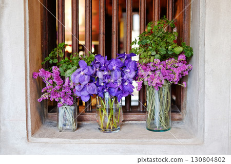 Blooming pink statice flower and violet orchid bouquet in clear glass vase on old wooden window grilles on holes in grunge concrete wall Blooming pink statice flower and violet orchid bouquet in clear glass vase on old wooden window grilles on holes in grunge concrete wall 130804802