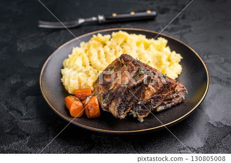 Braised beef short ribs resting on a bed of creamy mashed potatoes, creating an inviting culinary scene. black background. top view 130805008