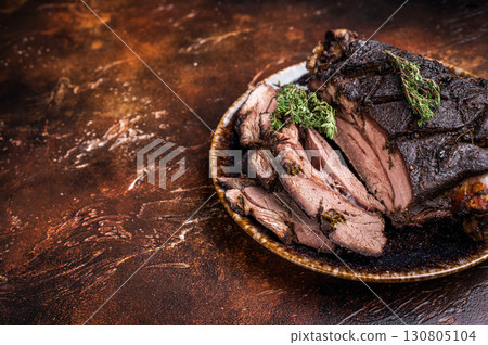Baked and sliced Venison leg. roast meat of deer with bone on a plate. brown background. top view 130805104