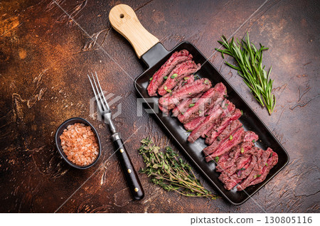 BBQ Grilled Flank beef steak, sliced meat with herbs, brown background. top view 130805116