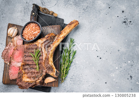 BBQ fried Tomahawk beef steak, grilled marbled rib eye with bone on wooden board. grey background. top view BBQ fried Tomahawk beef steak, grilled marbled rib eye with bone on wooden board. grey background. top view 130805238