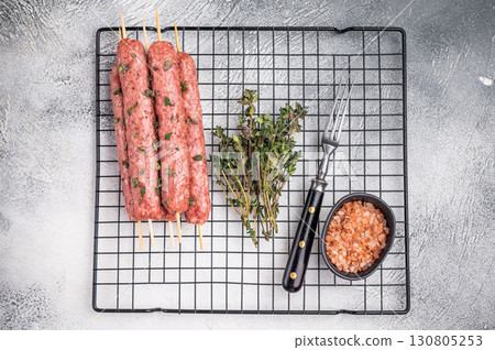 Raw kofta or lula kebabs skewers from mince lamb and beef meat on Skewer. grey background. top view Raw kofta or lula kebabs skewers from mince lamb and beef meat on Skewer. grey background. top view 130805253