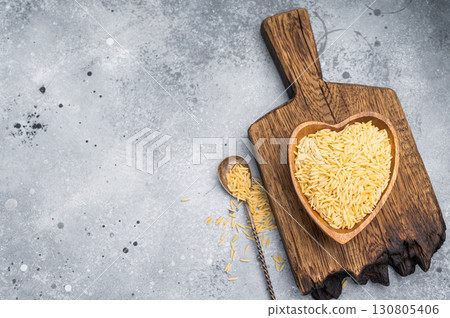 Raw Orzo pasta, uncooked dry Italian risoni in a bowl. grey background. top view Raw Orzo pasta, uncooked dry Italian risoni in a bowl. grey background. top view 130805406