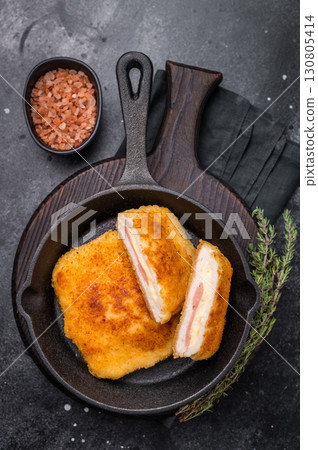 Fried cordon bleu cutlet with cheese and ham in pan. black background. top view Fried cordon bleu cutlet with cheese and ham in pan. black background. top view 130805414