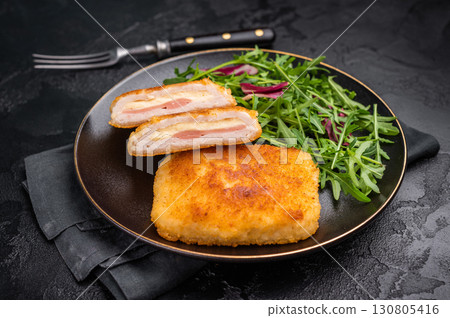 Chicken cordon bleu cutlet with cheese and ham on plate with salad. black background. top view Chicken cordon bleu cutlet with cheese and ham on plate with salad. black background. top view 130805416