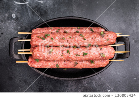 Raw shish kebab, arabic kofta kofte kebab from mince lamb and beef meat on Skewer. black background. top view Raw shish kebab, arabic kofta kofte kebab from mince lamb and beef meat on Skewer. black background. top view 130805424