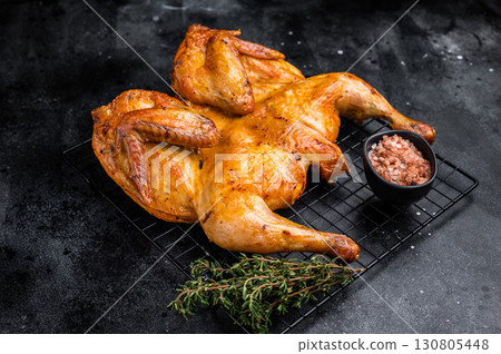 Roasted Spatchcock chicken with herbs and spices, poultry meat on steel rack. black background. top view 130805448