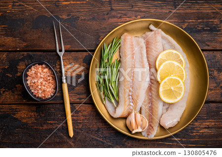 Pollock sea fish fillets, raw whitefish on a plate with herbs and lemon. wooden background. top view Pollock sea fish fillets, raw whitefish on a plate with herbs and lemon. wooden background. top view 130805476