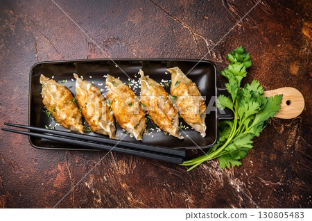 Fried Jiaozi on plate with sauce, Chinese Dumplings with shrimps and vegetables. brown background. top view Fried Jiaozi on plate with sauce, Chinese Dumplings with shrimps and vegetables. brown background. top view 130805483