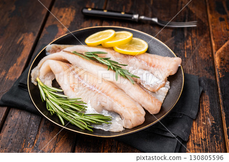 Organic Raw Haddock fish fillets, whitefish on a plate with herbs. wooden background. top view Organic Raw Haddock fish fillets, whitefish on a plate with herbs. wooden background. top view 130805596