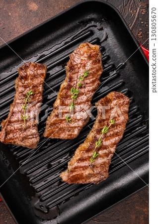 Grilled Tri tip steaks, marbled beef meat on pan with herbs. brown background. top view 130805670