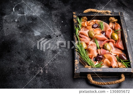 Prosciutto ham or Jamon Serrano with rosemary and olives in wooden tray. black background. top view Prosciutto ham or Jamon Serrano with rosemary and olives in wooden tray. black background. top view 130805672