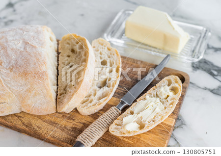 Sliced ciabatta bread with fresh butter on a wooden cutting board. marble background. top view Sliced ciabatta bread with fresh butter on a wooden cutting board. marble background. top view 130805751