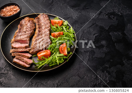 Grilled Steak from Black Angus beef meat on a plate with salad. black background. top view 130805824