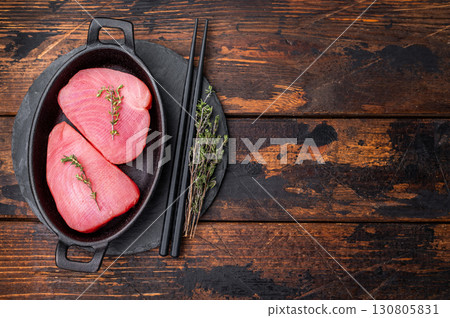 Vibrant raw tuna steak, showcasing its deep red hue, an essential ingredient for sushi enthusiasts and seafood connoisseurs. wooden background. top view 130805831