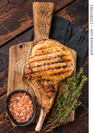 Tender grilled Tomahawk pork chop, showcasing its rich marbling and smoky aroma for a delightful dining experience. wooden background. top view Tender grilled Tomahawk pork chop, showcasing its rich marbling and smoky aroma for a delightful dining experience. wooden background. top view 130805861